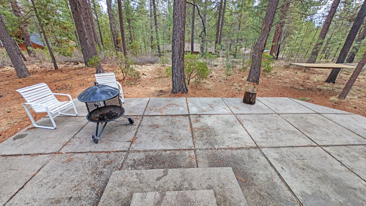 A cozy outdoor fire pit surrounded by white chairs, nestled among trees with a nearby hammock for lounging. The setup invites residents and guests to gather for campfire evenings, outdoor meals, and relaxation in a private, natural setting.