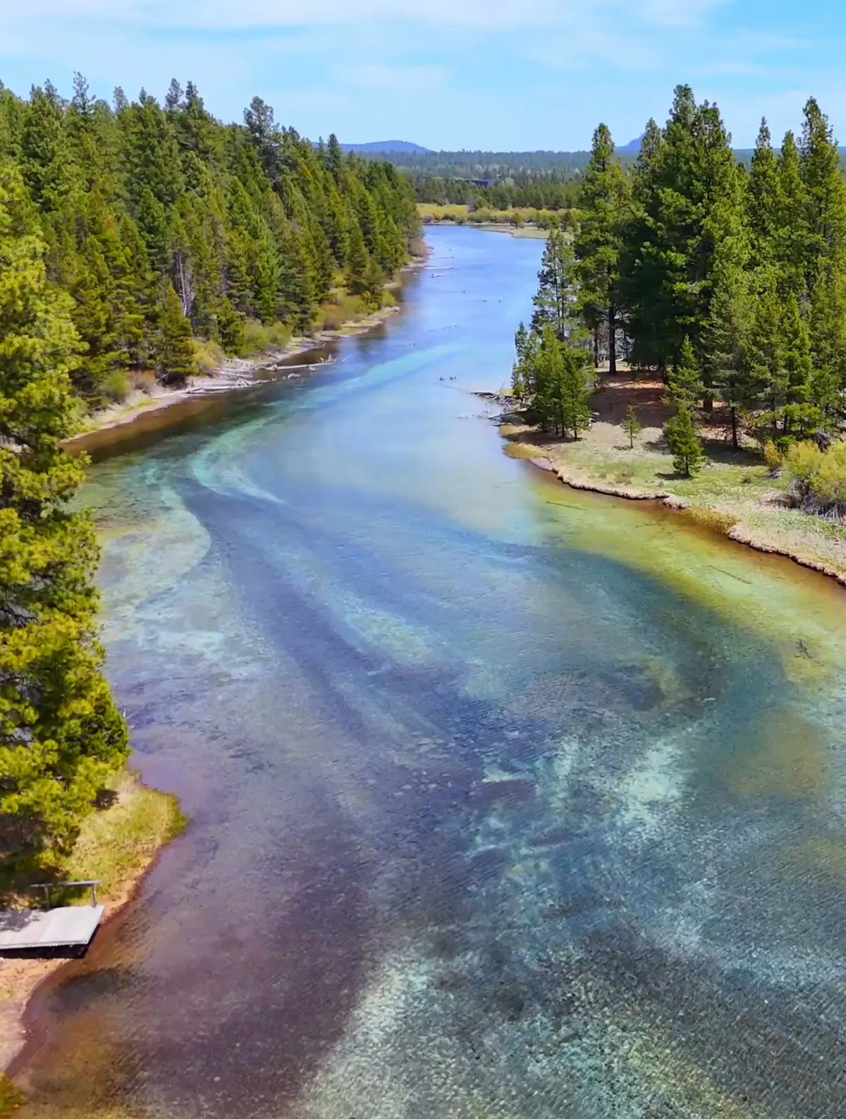 A scenic view of the river flanked by trees and distant hills, suggesting tranquility and opportunities for riverside activities like fishing, hiking, and picnicking.