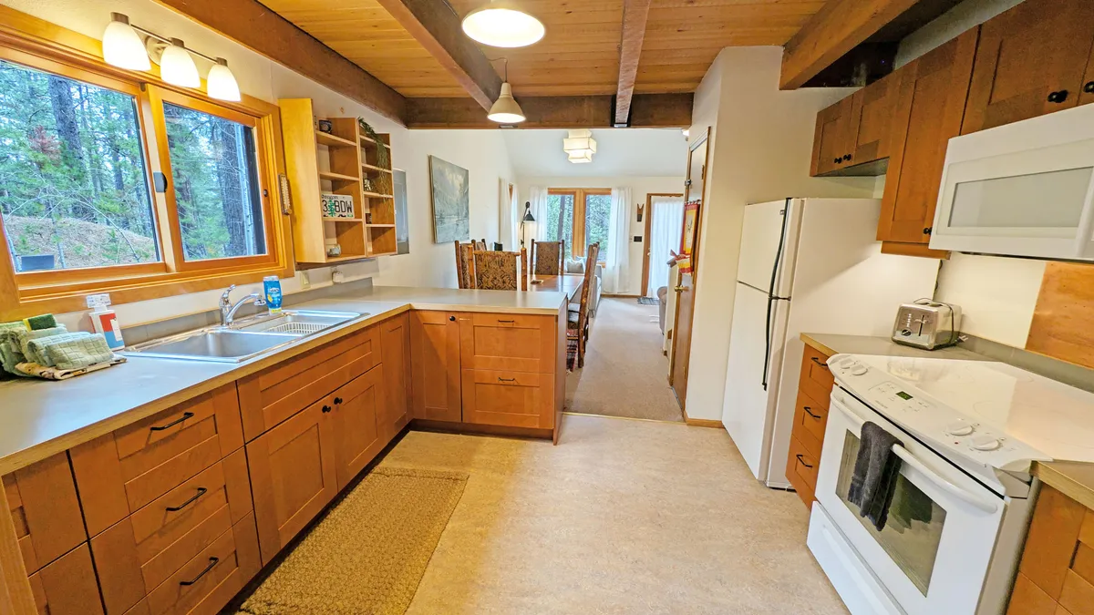 A cozy kitchen scene with a kitchen counter, sink, refrigerator, and a dining table, all framed in warm wood tones. The layout encourages both meal preparation and social interaction, reflecting the galley kitchen's role as a hub for home-cooked meals.
