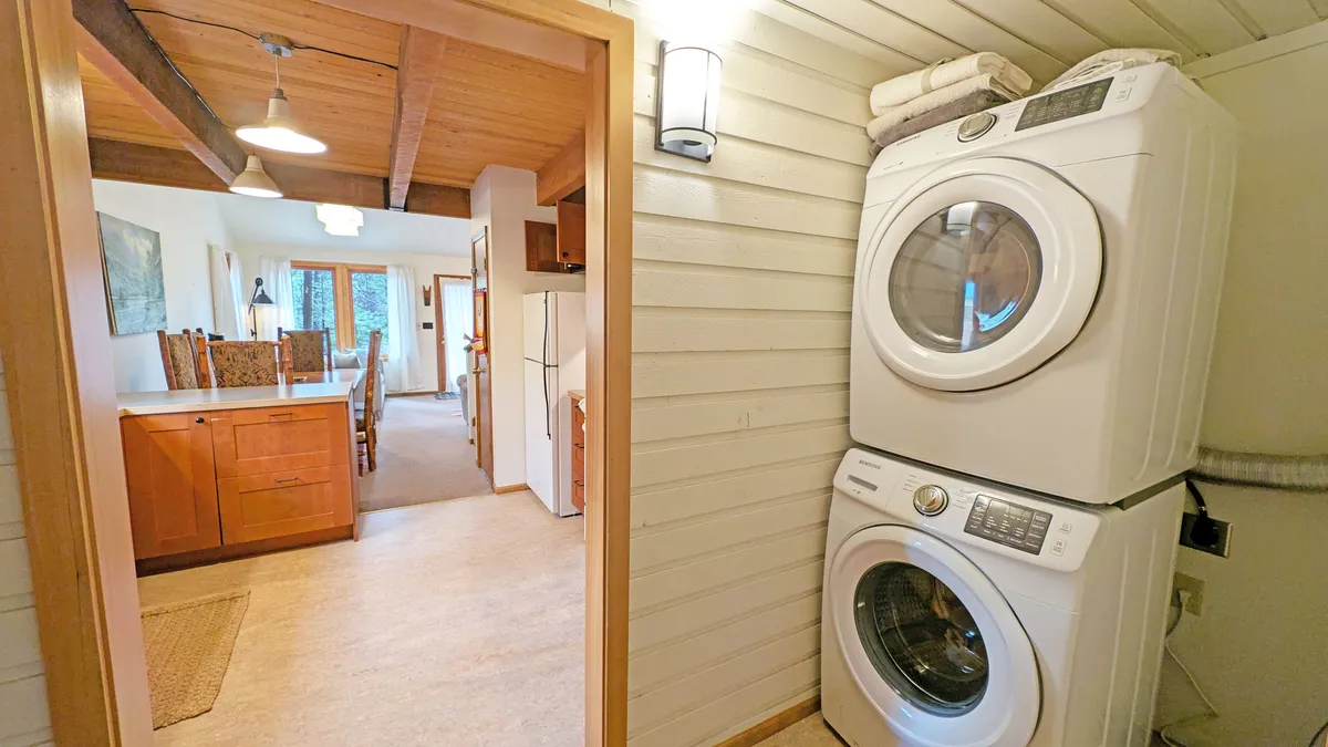This image offers a clear perspective on the entryway, showcasing the washer and dryer with warm wooden cabinetry and an adjacent dining area bathed in natural light. It illustrates both the practical aspect of laundry facilities and the welcoming atmosphere that greets guests upon entering.